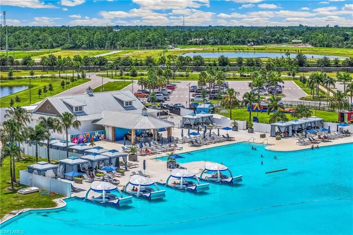 Lagoon-style pool with integrated sun shelves, expansive paved pool deck, shaded cabanas, and built-in poolside bar