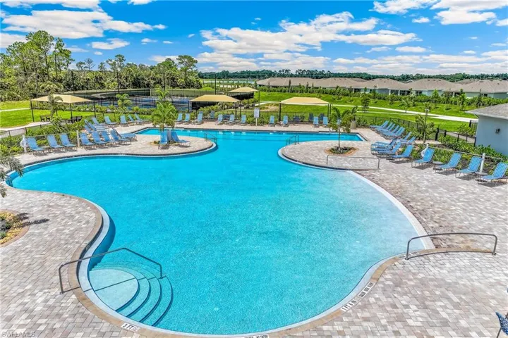 Expansive resort-style pool with multiple entry points, integrated tanning shelves, and surrounding paver decking