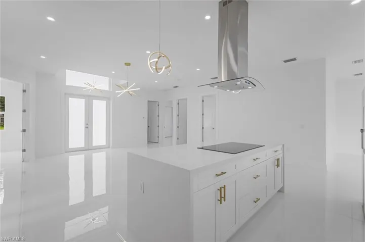 Kitchen featuring black electric stovetop, a center island, island exhaust hood, white cabinetry, and french doors