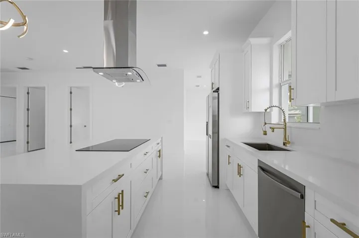 Kitchen with appliances with stainless steel finishes, island range hood, white cabinets, and sink