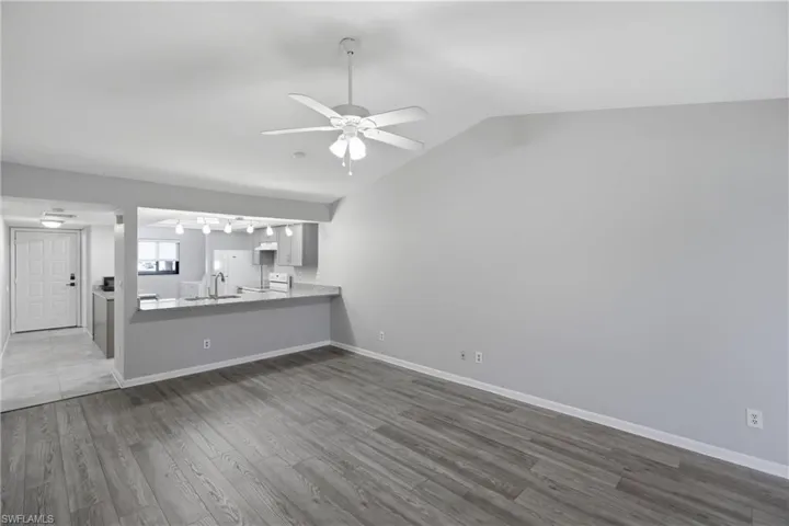 Unfurnished living room featuring dark wood-style floors, a ceiling fan, and lofted ceiling