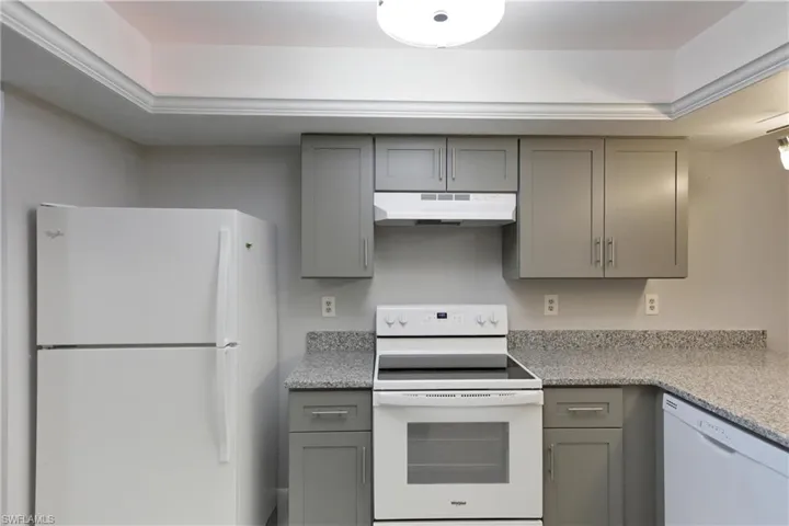 Kitchen with gray cabinetry, white appliances, light stone counters, and under cabinet range hood