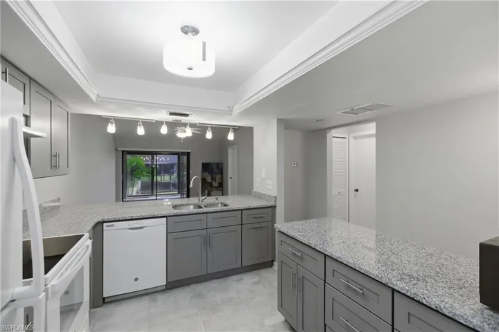 Kitchen featuring gray cabinetry, light stone countertops, and white appliances