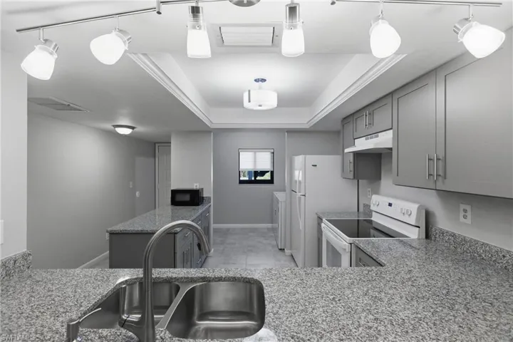 Kitchen featuring gray cabinetry, white range with electric stovetop, a raised ceiling, under cabinet range hood, and black microwave