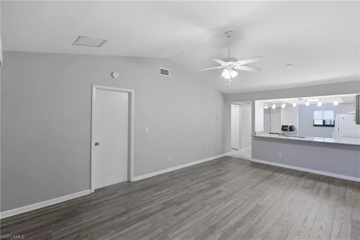 Unfurnished living room with dark wood-style flooring, lofted ceiling, a desk, and a ceiling fan