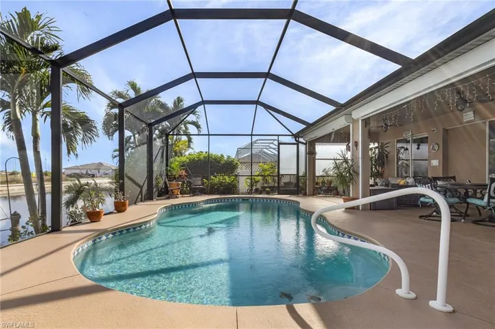 View of swimming pool with glass enclosure, a patio area, and a water view