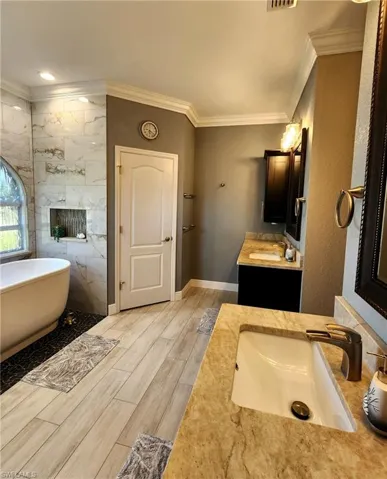 Bathroom featuring a tub to relax in, hardwood / wood-style flooring, vanity, tile walls, and ornamental molding