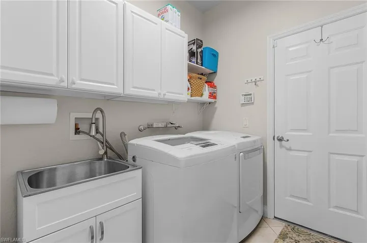 Clothes washing area featuring washer and dryer, light tile patterned flooring, cabinets, and sink