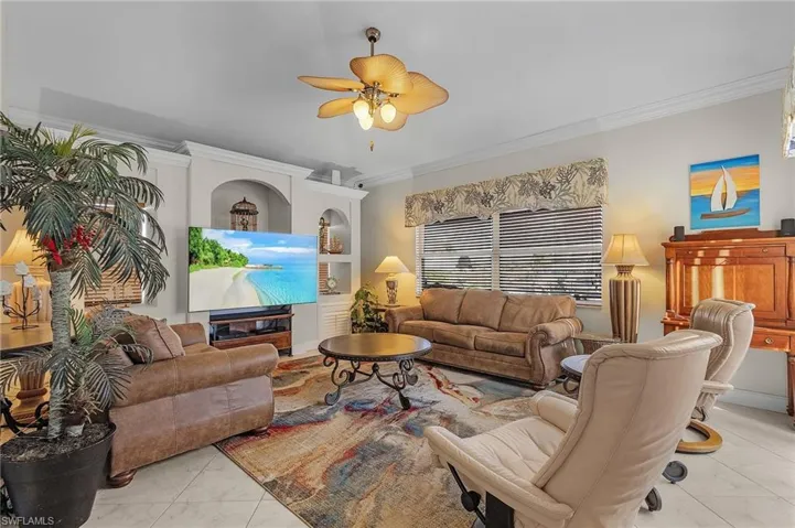 Living room with light tile patterned floors, ceiling fan, and ornamental molding