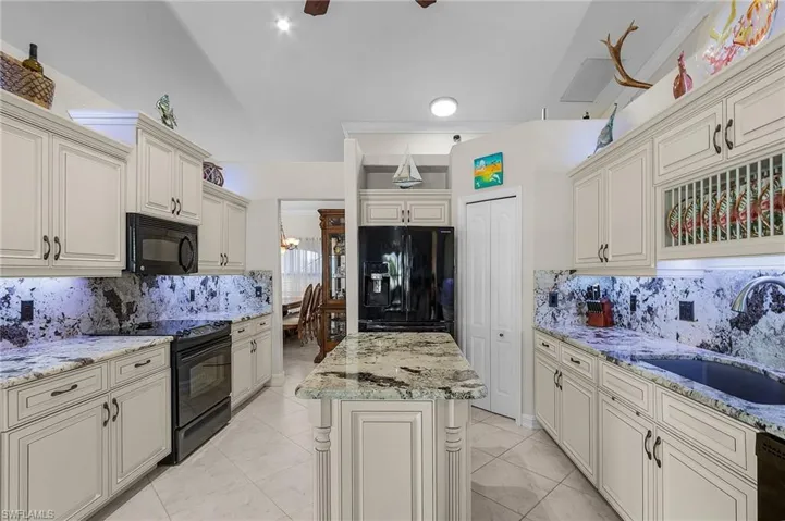 Kitchen featuring tasteful backsplash, light stone countertops, sink, and black appliances