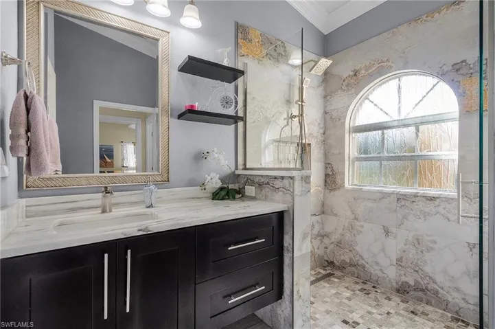Bathroom featuring tiled shower, vanity, and crown molding