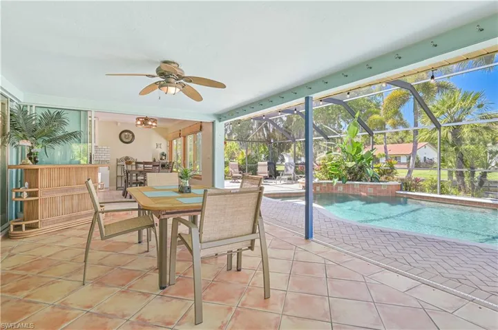 The property features an outdoor patio area with tiled flooring and a ceiling fan, overlooking a screened-in swimming pool with a paved deck