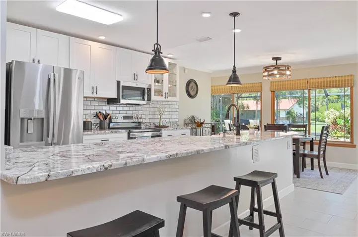 The kitchen features a spacious counter with seating, white cabinetry, stainless steel appliances, and a subway tile backsplash