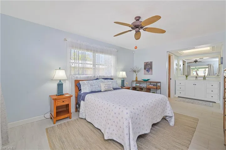This bedroom features light blue walls, a ceiling fan, and a window with blinds and sheer curtains