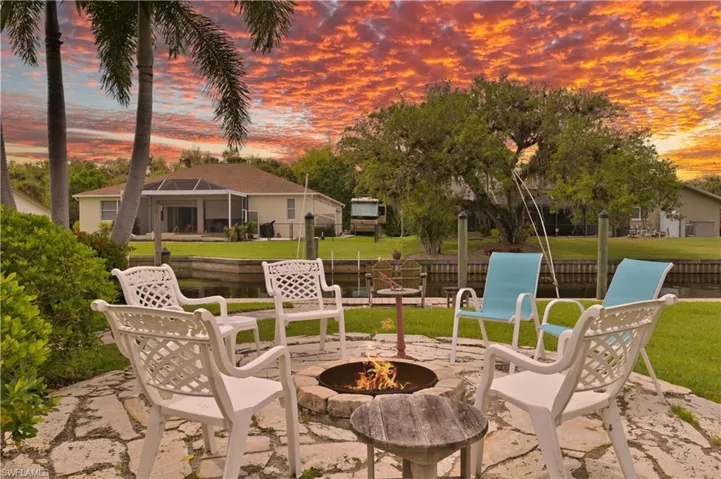 The property features a stone patio with a fire pit, overlooking a canal with boat pilings