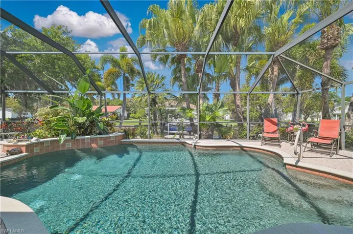 The property features a screened-in swimming pool area with a paved deck, surrounded by lush green foliage and palm trees