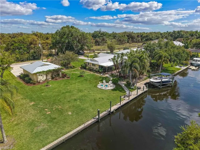 This property features a spacious green lawn, a private dock with a boat lift, and a charming paved patio area with outdoor seating