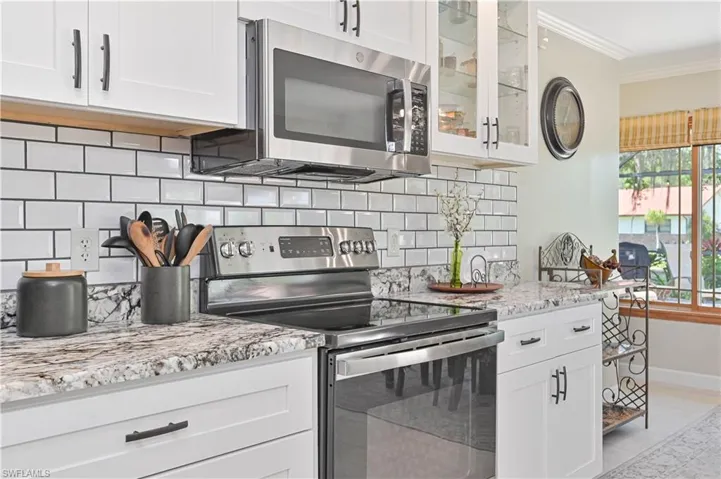 The kitchen features white cabinetry with black hardware, granite countertops, a white subway tile backsplash, and stainless steel appliances including a microwave and range