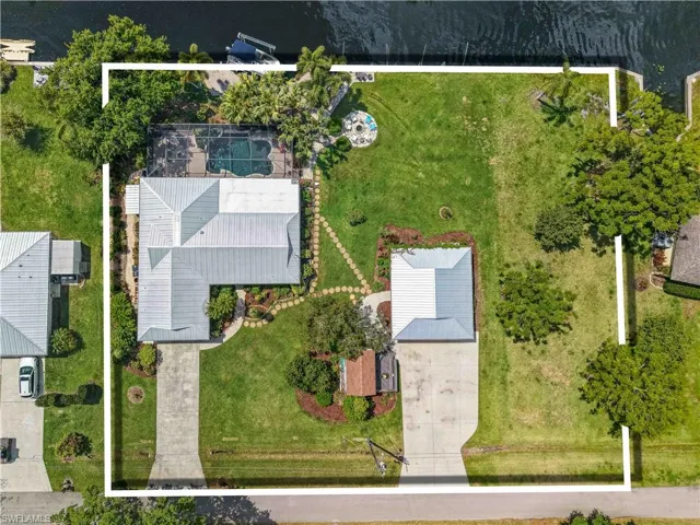 Aerial view showcasing the property's expansive lot with a private pool and patio area, a detached structure with a driveway, and waterfront access