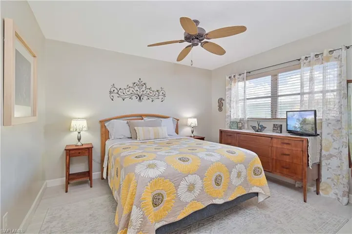 The property features a bedroom with a ceiling fan, a window with blinds and sheer curtains, and light-colored flooring