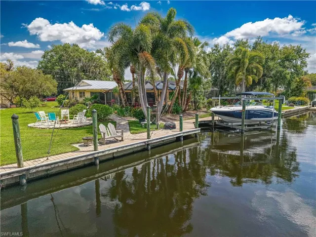 The property features a private dock with a boat lift, a spacious grassy yard with a fire pit area, and mature palm trees