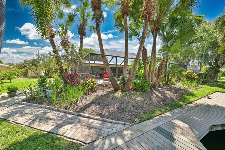 The property features a screened-in lanai, mature palm trees, a well-maintained lawn, and a paved walkway