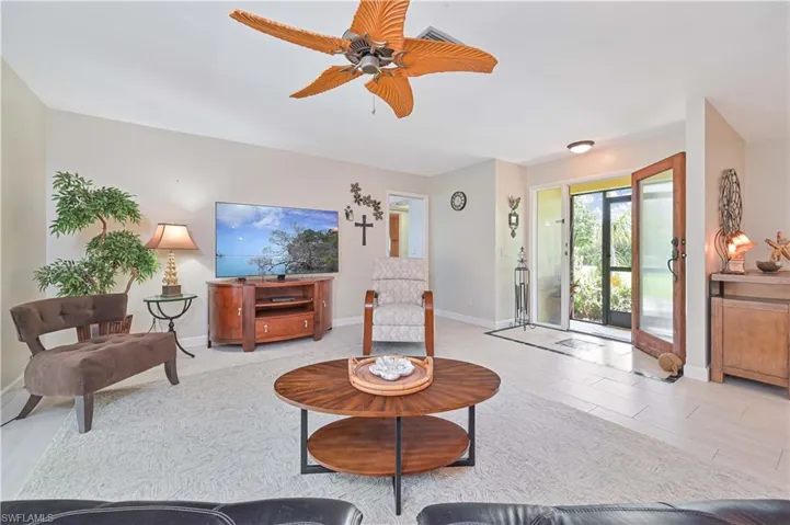 The spacious living area features a ceiling fan, light-colored flooring, and a glass-paneled entry door