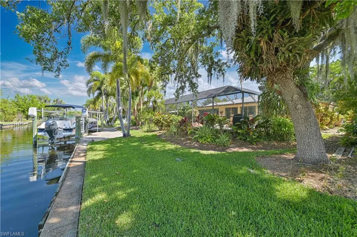 This property features a boat dock with a boat lift on a canal, a well-maintained lawn, and mature trees with Spanish moss
