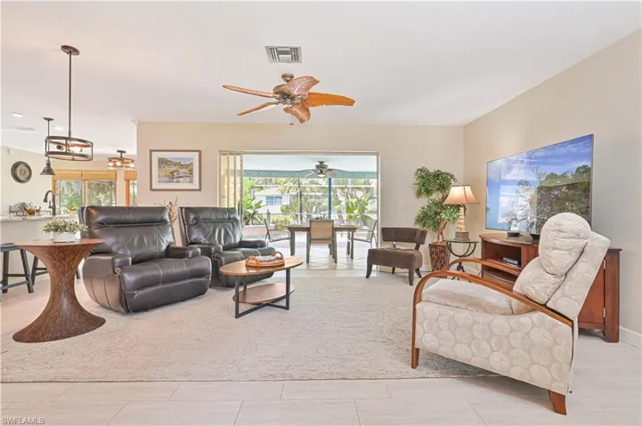 Spacious living area featuring light-colored flooring, a ceiling fan, and large sliding glass doors opening to an outdoor patio with a view of lush greenery