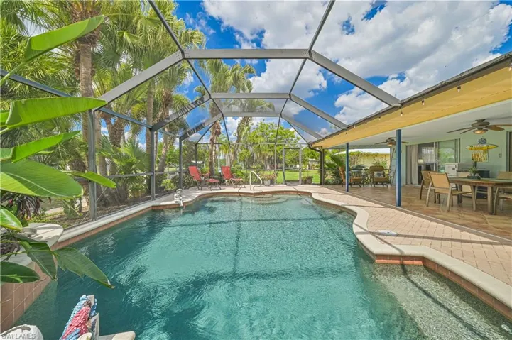 Expansive screened-in pool area featuring a clear blue pool, paver deck, and a covered lanai with outdoor dining space
