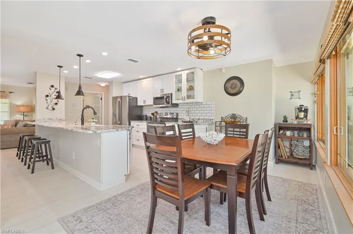 This open-plan kitchen and dining area features white cabinetry, a tiled backsplash, and stainless steel appliances