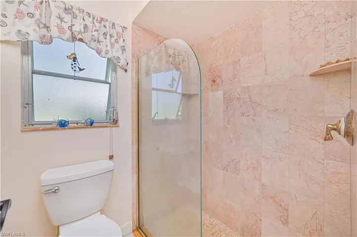 The bathroom features a toilet, a shower with a glass enclosure, and walls tiled with natural stone
