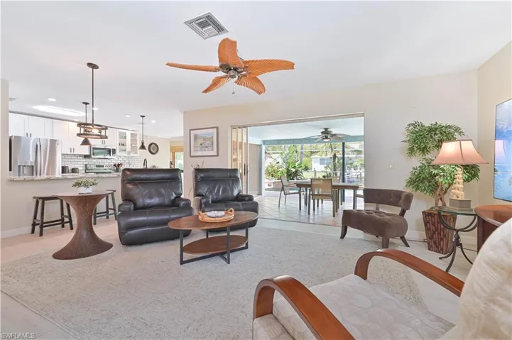 The open concept living area features a ceiling fan, light-colored flooring, and provides an open view to the kitchen area with stainless steel appliances and a breakfast bar