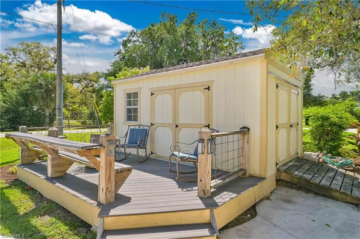 Detached shed with light yellow siding, a window, and a gray deck featuring a built-in picnic table and railing