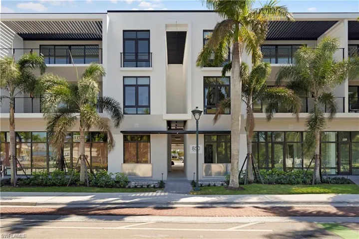 Modern building facade featuring large format windows, multiple balconies with black railings, and an integrated overhead pergola