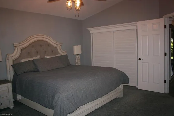 Vaulted ceiling with a ceiling fan, light gray wall paint, white louvered closet doors, and dark carpet flooring