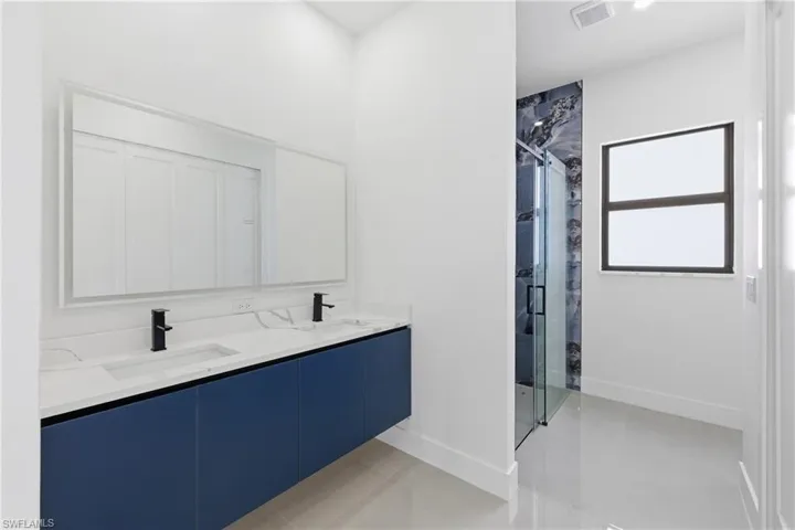 Full bath with a marble finish shower, double vanity, and light tile patterned floors