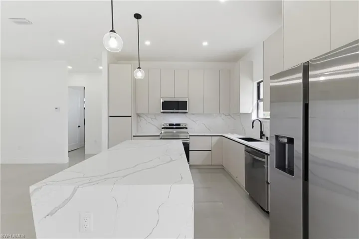 Kitchen with stainless steel appliances, modern cabinets, light stone countertops, a kitchen island, and hanging light fixtures