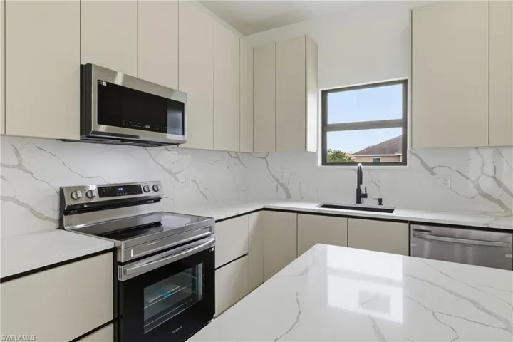 Kitchen featuring stainless steel appliances, light stone counters, decorative backsplash, and modern cabinets