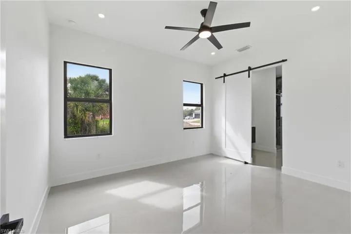 Unfurnished bedroom featuring a barn door, a ceiling fan, and recessed lighting
