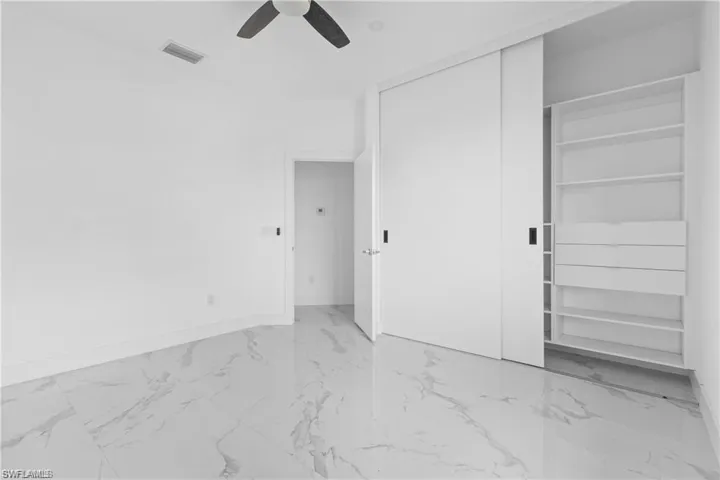 Unfurnished bedroom with light marble finish floors, ceiling fan, and a closet