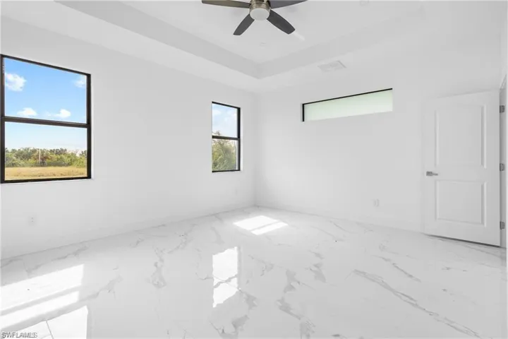 Unfurnished room with light marble finish flooring, a raised ceiling, and ceiling fan