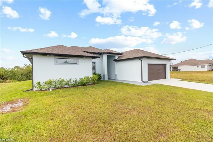 Prairie-style house with concrete driveway, a front yard, an attached garage, stucco siding, and roof with shingles