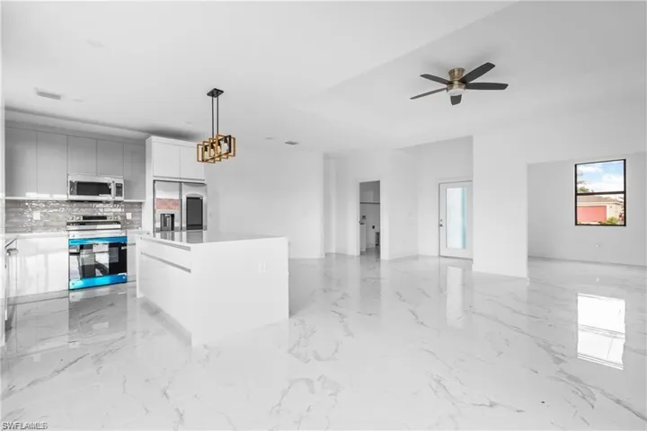Kitchen featuring stainless steel appliances, a center island, decorative light fixtures, and light marble finish flooring
