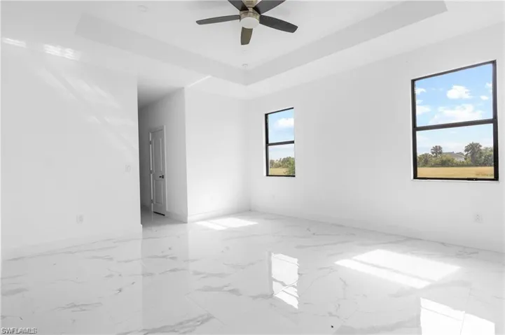 Unfurnished room featuring a tray ceiling, light marble finish flooring, and a ceiling fan