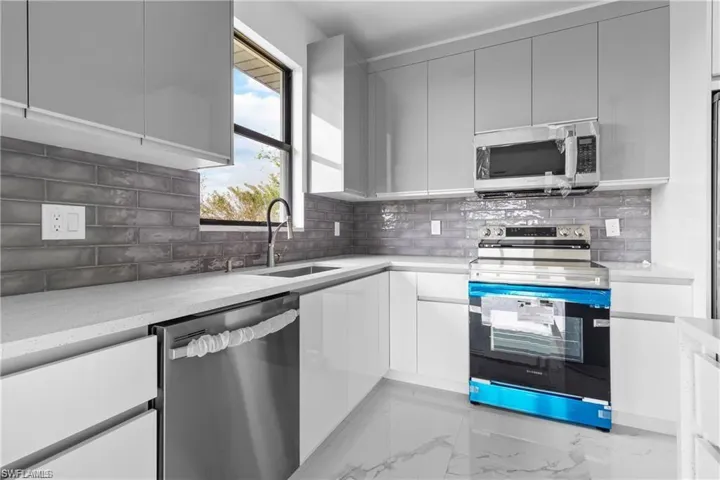 Kitchen featuring appliances with stainless steel finishes, modern cabinets, tasteful backsplash, light marble finish floors, and light stone countertops