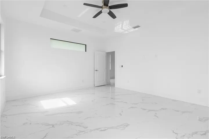 Unfurnished room featuring light marble finish floors, a raised ceiling, and ceiling fan