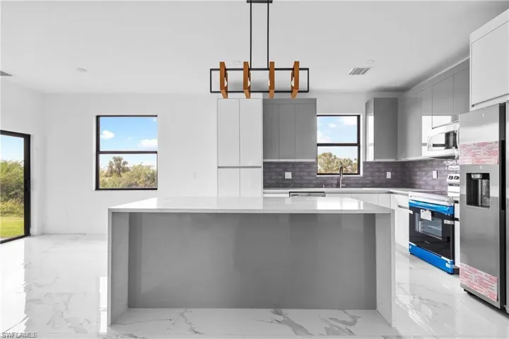 Kitchen with light marble finish flooring, decorative backsplash, stainless steel appliances, modern cabinets, and hanging light fixtures
