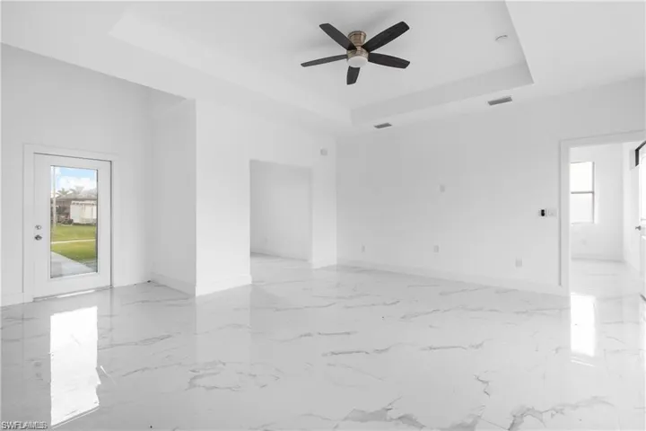 Empty room with a tray ceiling, light marble finish flooring, and a ceiling fan