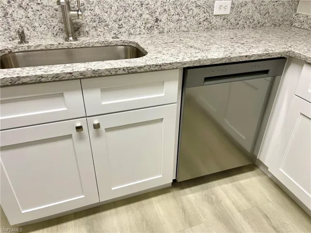 Modern kitchen featuring a brand-new dishwasher, complemented by light stone countertops, crisp white cabinets, and warm, light wood-style flooring.